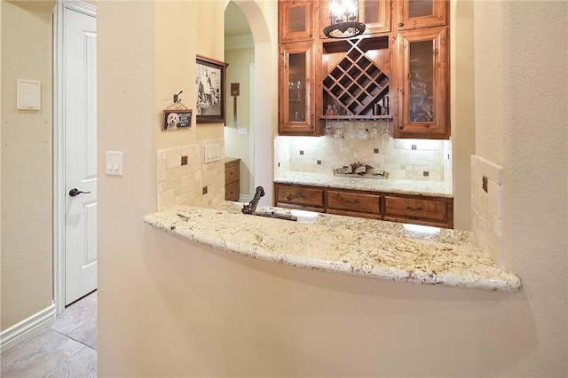 bar with tasteful backsplash, sink, light tile patterned floors, and light stone counters