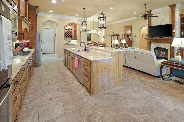 kitchen featuring appliances with stainless steel finishes, a fireplace, sink, hanging light fixtures, and a center island with sink