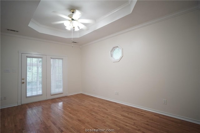 empty room with wood-type flooring, a raised ceiling, ceiling fan, and ornamental molding