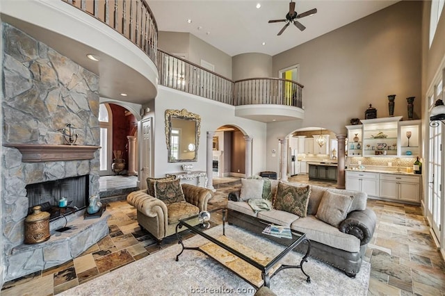 living room featuring ceiling fan, a stone fireplace, and a high ceiling