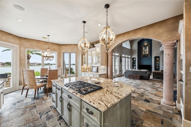 kitchen featuring light stone countertops, decorative columns, a water view, a kitchen island, and hanging light fixtures