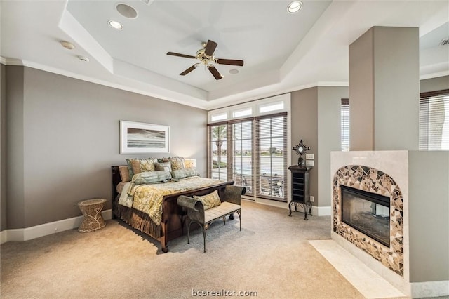 carpeted bedroom with a tray ceiling, ceiling fan, crown molding, and a tiled fireplace