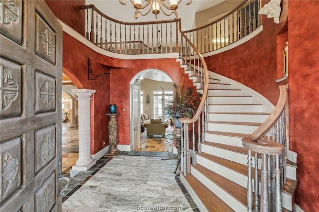 foyer featuring a chandelier, a towering ceiling, and ornate columns