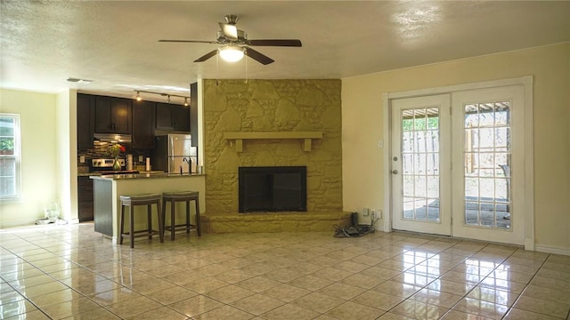 living room featuring ceiling fan, a fireplace, light tile patterned floors, and a textured ceiling