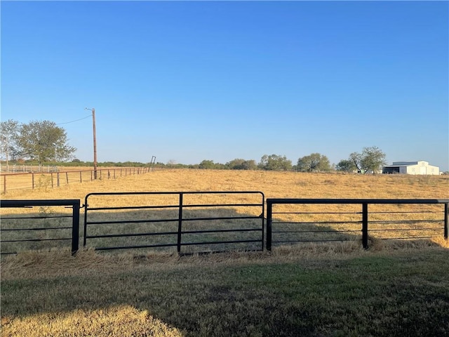 view of gate with a lawn and a rural view