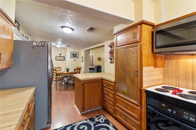 10072 Riley Green Rd, Franklin, TX 77856 - kitchen featuring stainless steel appliances, a peninsula, light countertops, light wood-type flooring, and brown cabinets