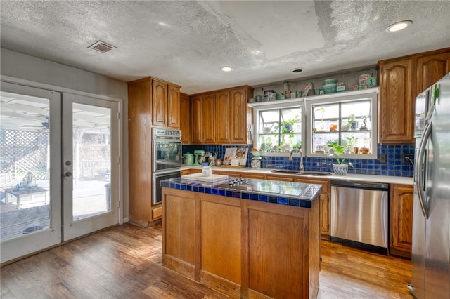 kitchen with french doors, sink, light hardwood / wood-style flooring, appliances with stainless steel finishes, and a kitchen island