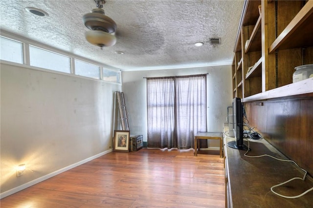 unfurnished office featuring wood-type flooring, ornamental molding, a healthy amount of sunlight, and a textured ceiling