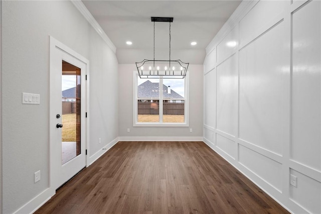 unfurnished dining area featuring dark wood-type flooring, crown molding, and a chandelier