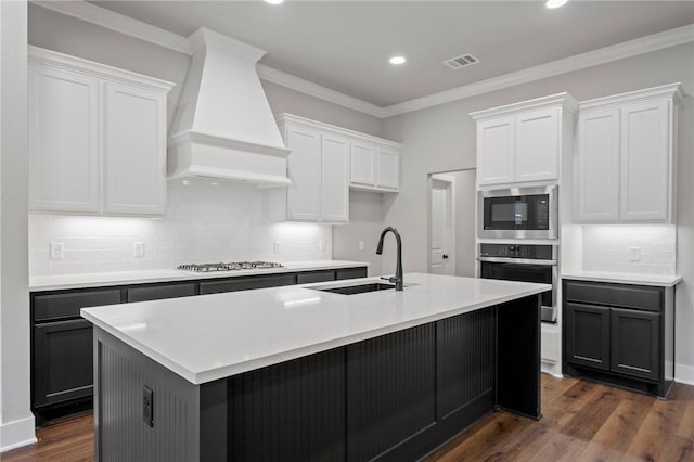 kitchen featuring white cabinets, a kitchen island with sink, stainless steel appliances, and custom range hood