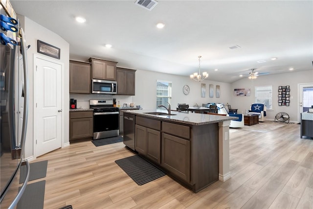 kitchen with decorative light fixtures, a center island with sink, light wood-type flooring, appliances with stainless steel finishes, and ceiling fan with notable chandelier