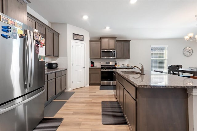 kitchen featuring sink, an inviting chandelier, light wood-type flooring, appliances with stainless steel finishes, and an island with sink