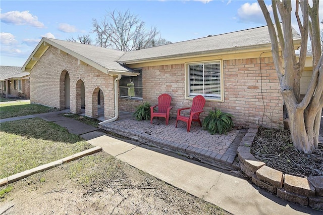 exterior space with brick siding, a front yard, and a patio