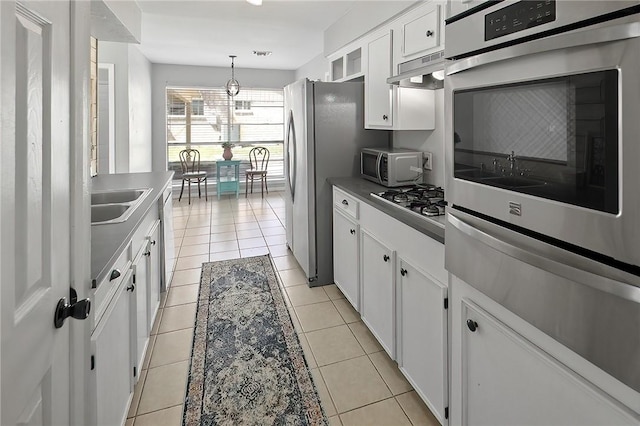 kitchen with light tile patterned floors, stainless steel appliances, hanging light fixtures, under cabinet range hood, and white cabinetry