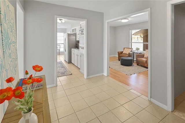 hall with light tile patterned floors, a healthy amount of sunlight, and baseboards