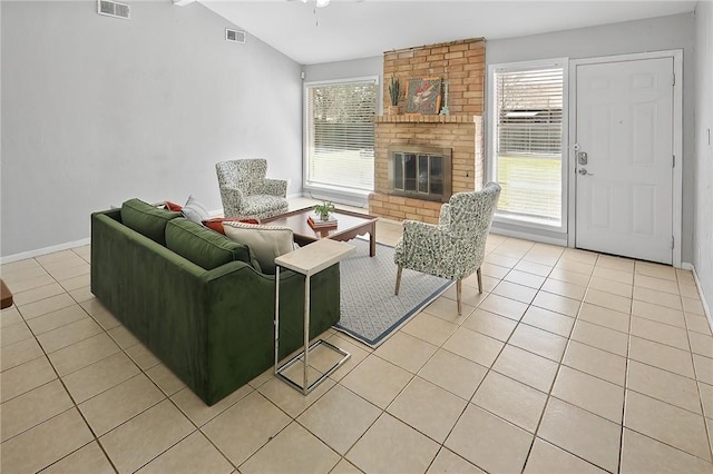 living area featuring vaulted ceiling, a brick fireplace, light tile patterned floors, and visible vents