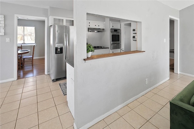 kitchen featuring baseboards, under cabinet range hood, appliances with stainless steel finishes, light tile patterned flooring, and white cabinets