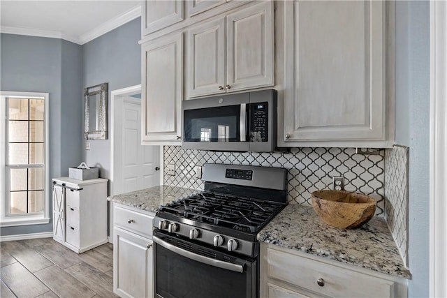 kitchen with white cabinetry, stainless steel appliances, backsplash, light wood-type flooring, and ornamental molding