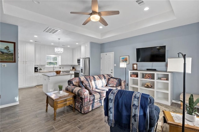 living room featuring a raised ceiling, sink, light hardwood / wood-style floors, and ceiling fan with notable chandelier