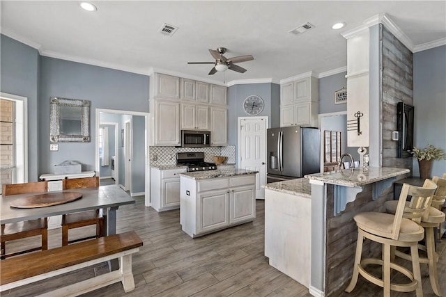 kitchen featuring ornamental molding, appliances with stainless steel finishes, light hardwood / wood-style floors, light stone counters, and kitchen peninsula