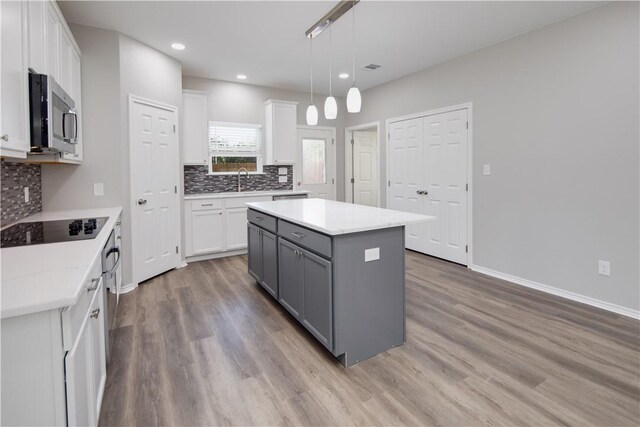 507 Brosig Ave, Navasota, TX 77868 - kitchen with stainless steel microwave, gray cabinets, black electric cooktop, white cabinets, and light wood-type flooring