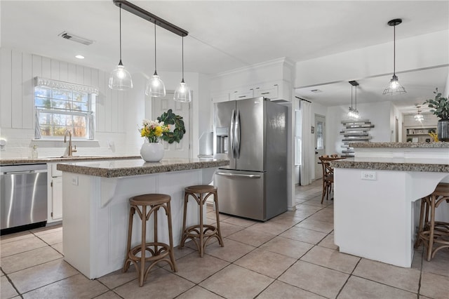 kitchen with appliances with stainless steel finishes, pendant lighting, white cabinets, a kitchen bar, and a center island