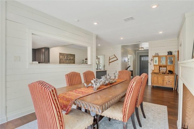 dining room with recessed lighting, visible vents, wooden walls, and dark wood finished floors