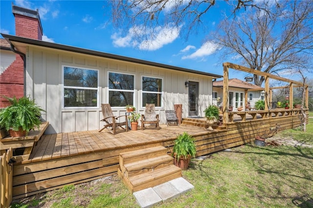 rear view of house featuring a lawn, a chimney, board and batten siding, and a wooden deck