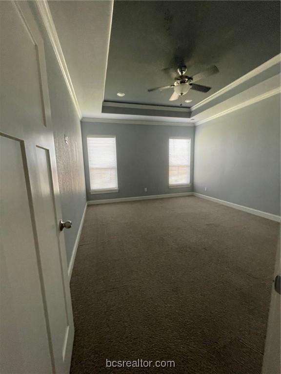 empty room featuring carpet flooring, a tray ceiling, ceiling fan, and crown molding