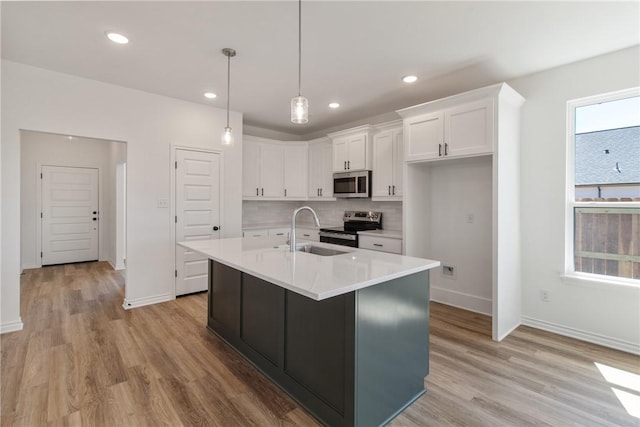 kitchen featuring a kitchen island with sink, sink, light wood-type flooring, appliances with stainless steel finishes, and white cabinetry