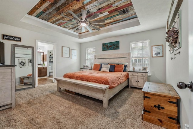 carpeted bedroom with a raised ceiling, connected bathroom, and multiple windows