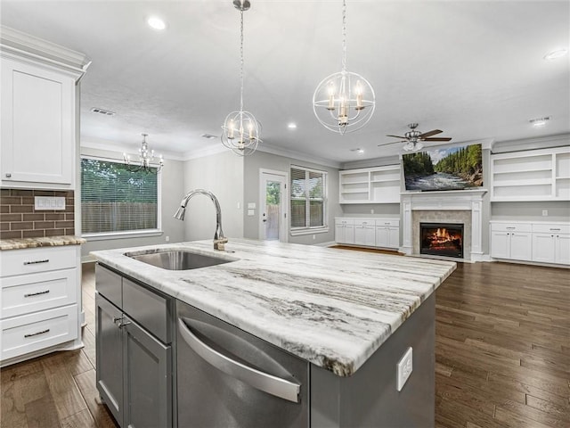 kitchen with white cabinetry, sink, light stone counters, a kitchen island with sink, and ceiling fan with notable chandelier