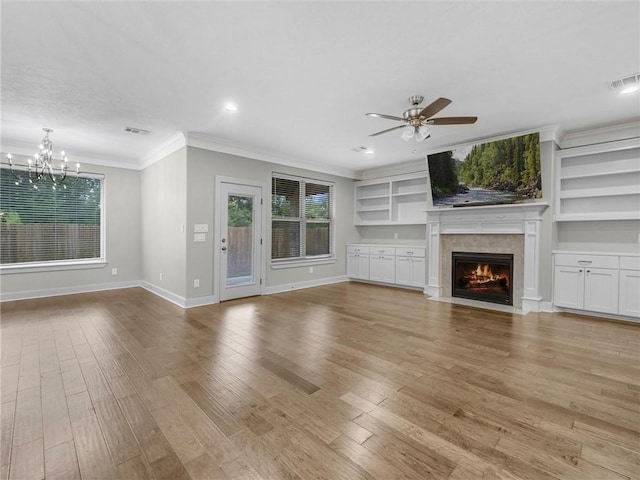 unfurnished living room with built in shelves, crown molding, a high end fireplace, and light hardwood / wood-style flooring