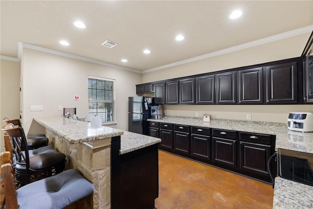 kitchen featuring finished concrete flooring, dark cabinets, freestanding refrigerator, a kitchen bar, and recessed lighting