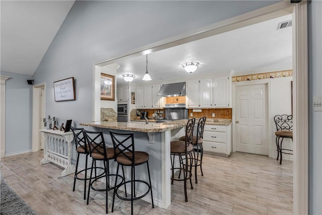 3003 Aztec St, College Station, TX 77845 - kitchen with wall chimney exhaust hood, a kitchen breakfast bar, lofted ceiling, white cabinetry, and a peninsula
