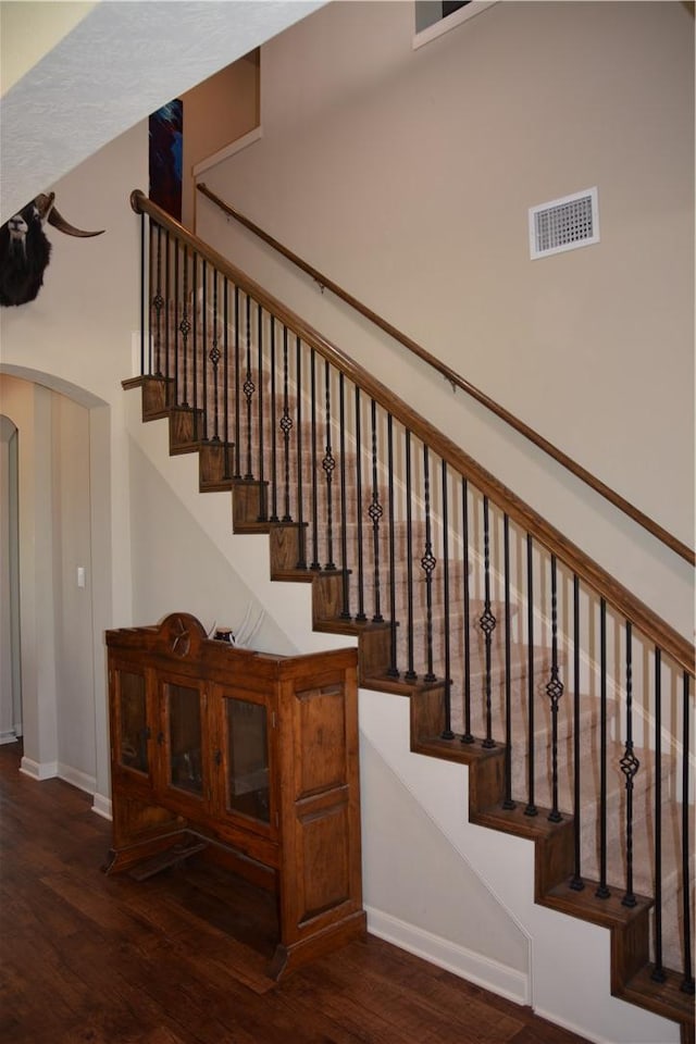stairway with baseboards, arched walkways, wood finished floors, and visible vents