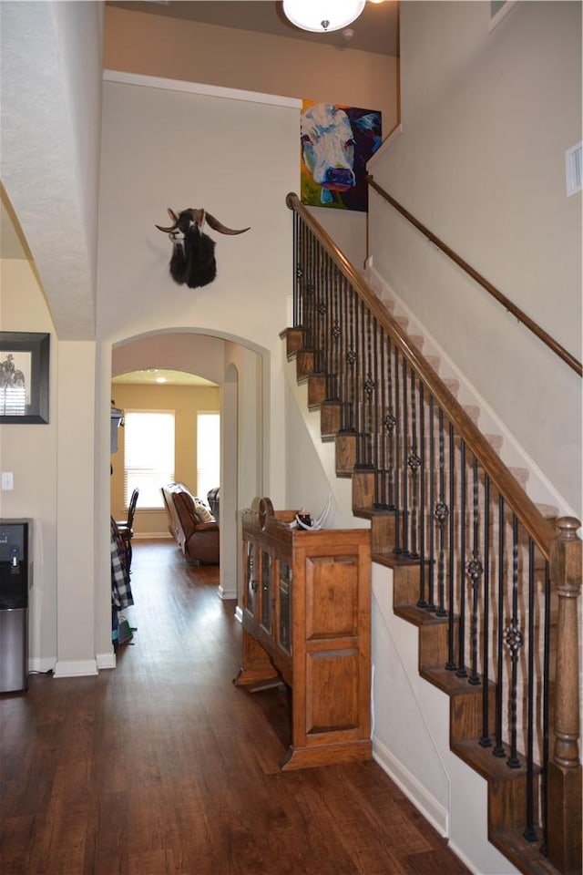 stairway featuring arched walkways, baseboards, and wood finished floors