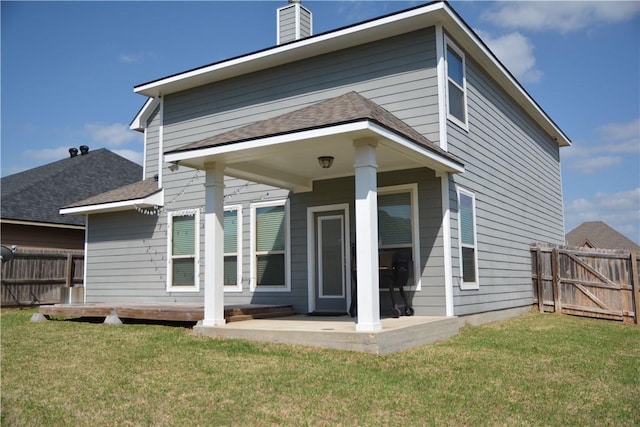 rear view of property featuring fence, a chimney, a shingled roof, a patio area, and a lawn
