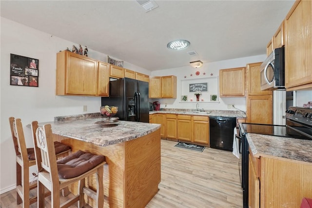 kitchen with black appliances, kitchen peninsula, a kitchen bar, sink, and light hardwood / wood-style flooring