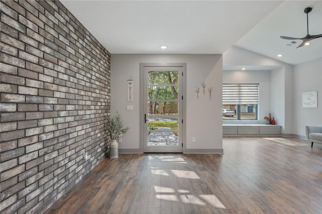 interior space featuring ceiling fan, dark wood-type flooring, brick wall, and lofted ceiling