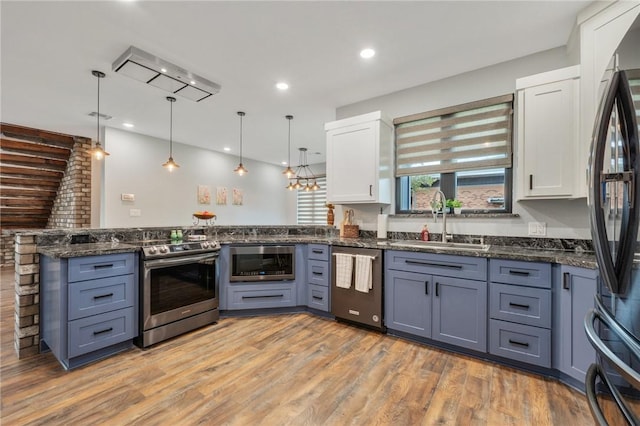 kitchen featuring a peninsula, a sink, white cabinets, appliances with stainless steel finishes, and decorative light fixtures