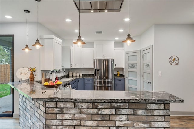 kitchen with a sink, visible vents, white cabinets, stainless steel fridge, and decorative light fixtures