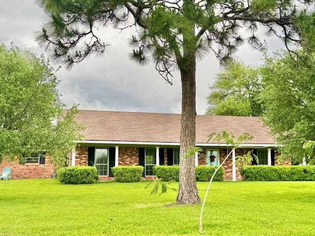 ranch-style home featuring brick siding, a front lawn, and roof with shingles