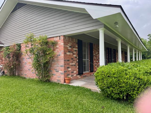 view of side of property with covered porch, a yard, and brick siding