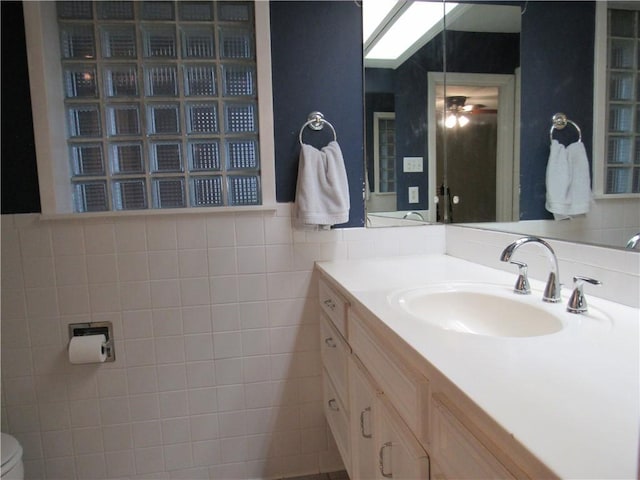 bathroom featuring toilet, tile walls, ceiling fan, and vanity