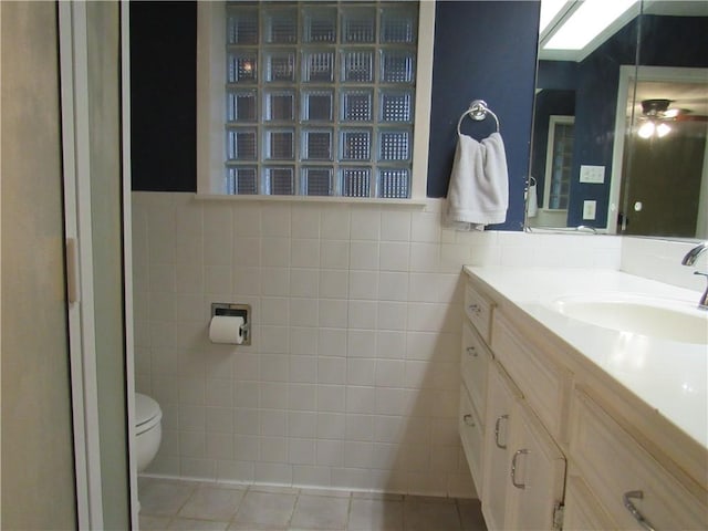 bathroom with tile patterned floors, tile walls, ceiling fan, toilet, and vanity