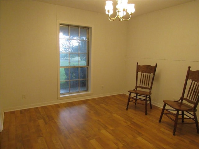 unfurnished room with an inviting chandelier, wood finished floors, and baseboards