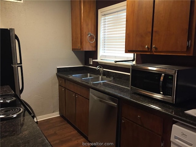 kitchen featuring appliances with stainless steel finishes, dark hardwood / wood-style floors, dark stone countertops, and sink