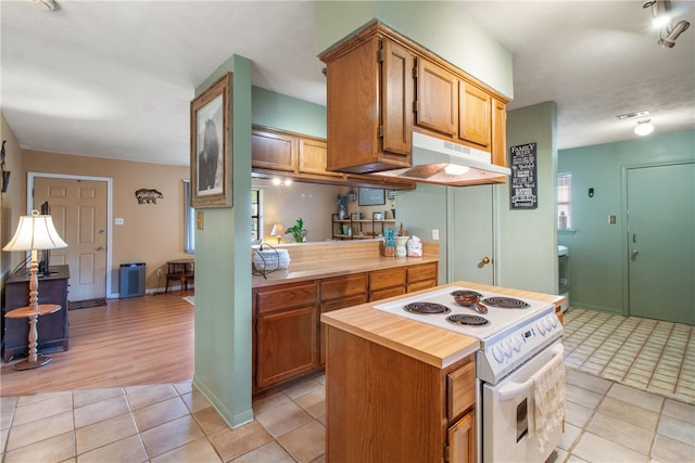 9777 Deer Trail Run, Hearne, TX 77859 - kitchen with electric range, under cabinet range hood, light tile patterned floors, brown cabinetry, and a kitchen island