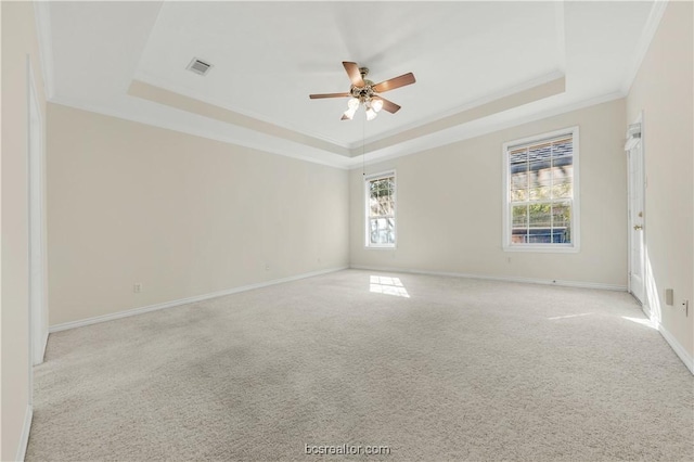 empty room featuring ornamental molding, a tray ceiling, visible vents, and light colored carpet